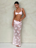 A woman stands against a plain background, wearing a light pink bralette with jeweled detail by Tiger Mist and the Xadie Skirt from TIGERMIST in pastel pink. Her hair is pulled back, and she accessorizes with small earrings and a pendant necklace.